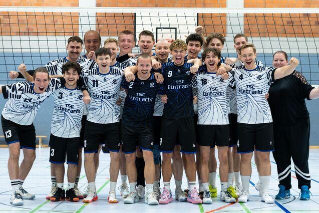 Gruppe von Volleyballspielern in einheitlichen Trikots lächelt und posiert freudig auf dem Spielfeld.