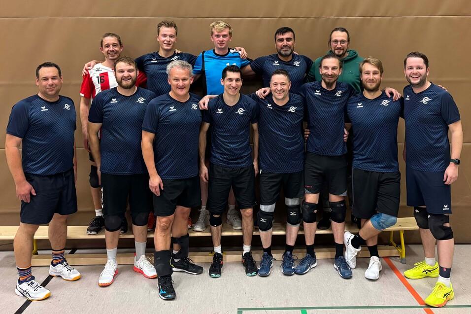 Gruppe von zehn m&auml;nnlichen Volleyballspielern in Sportkleidung, l&auml;chelnd und poses auf einem Hallenboden.