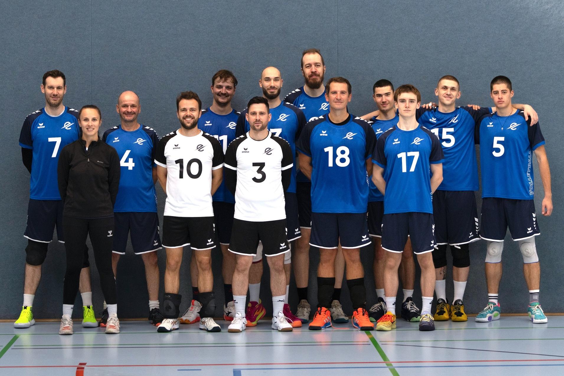Gruppenzusammenstellung von Volleyballspielern in blauer Teamkleidung, vor einem Volleyballnetz, mit Bällen in den Händen.