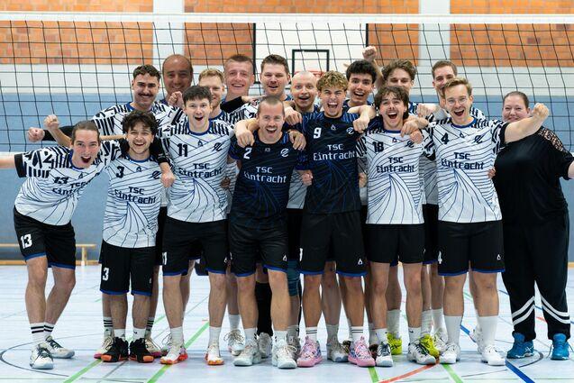 Gruppe von Volleyballspielern in einheitlichen Trikots lächelt und posiert freudig auf dem Spielfeld.