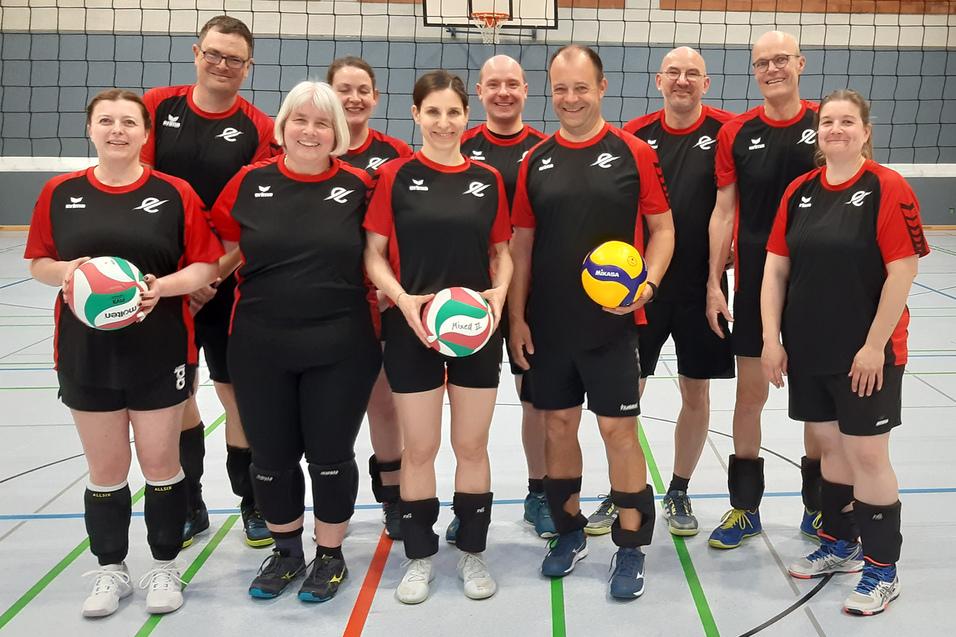 Gruppe von zehn Volleyballspielern in schwarz-roten Trikots, posierend auf einem Sportfeld mit B&auml;llen in der Hand.