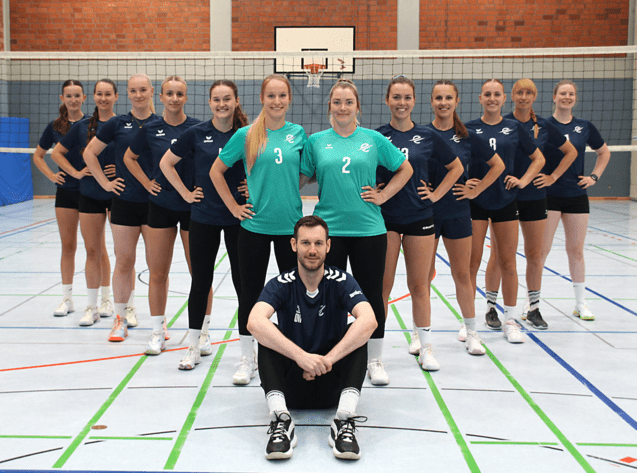 Gruppenfoto des Volleyballteams TSC Eintracht Dortmund vor dem Vereinsgeb&auml;ude, Spielerinnen in blau und gr&uuml;n, l&auml;chelnd.