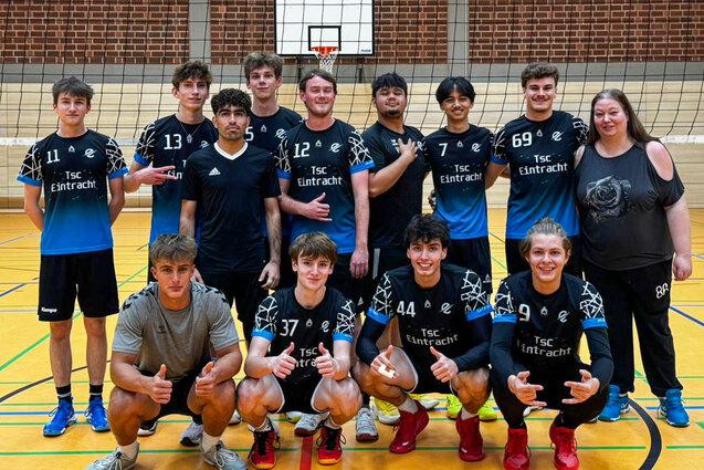Gruppennfoto einer Handballmannschaft mit zehn Spielern und einer Trainerin in Sportkleidung in einer Halle.