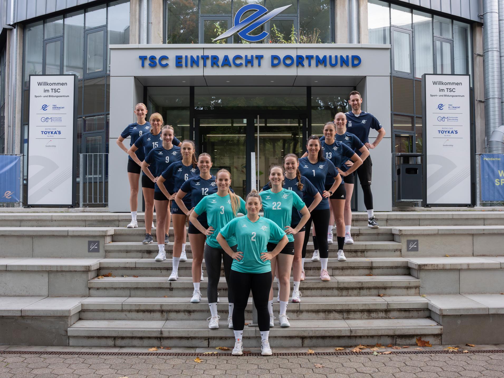 Gruppenfoto von elf weiblichen Volleyballspielerinnen in Vereinskleidung vor dem TSC Eintracht Dortmund, auf Treppenstufen stehend.
