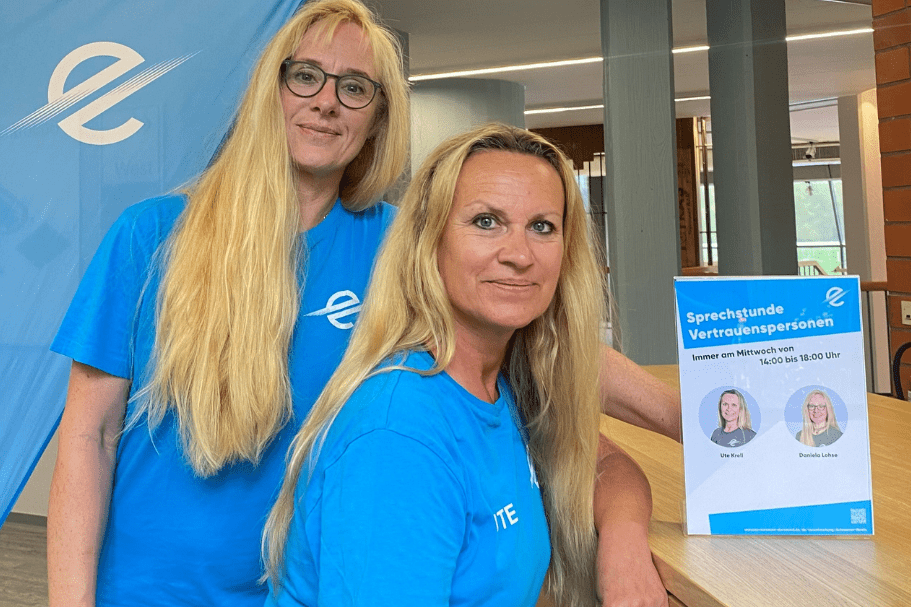 Zwei Frauen in blauen T-Shirts stehen an einem Tisch, neben einer Informationsbrosch&uuml;re und einem blauem Fahne.