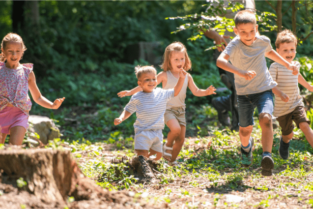 F&uuml;nf Kinder rennen fr&ouml;hlich durch einen sonnendurchfluteten Wald.