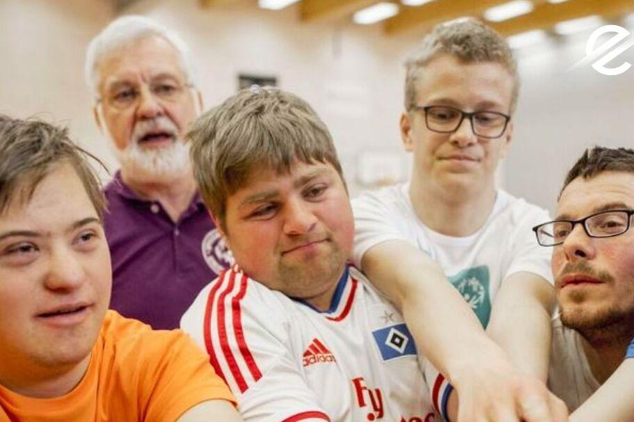 Sechs Personen mit unterschiedlichen Beeinträchtigungen bilden eine Gruppe und legen ihre Hände gemeinsam in die Mitte.