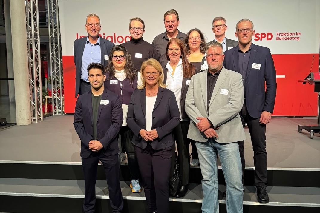 Gruppenfoto von zwölf Personen auf einer Bühne, alle lächelnd vor einem Hintergrund mit SPD-Logo.
