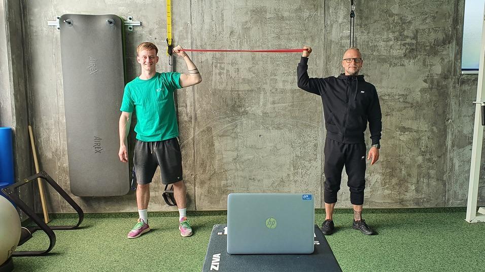Zwei Männer führen ein Training mit Widerstandsbändern in einem modern gestalteten Fitnessraum durch.