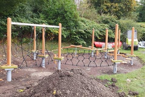 Neuer Spielplatz mit Klettergerüst, Schaukeln und einer Rutsche in einer grünen Umgebung, frisch geordnet.