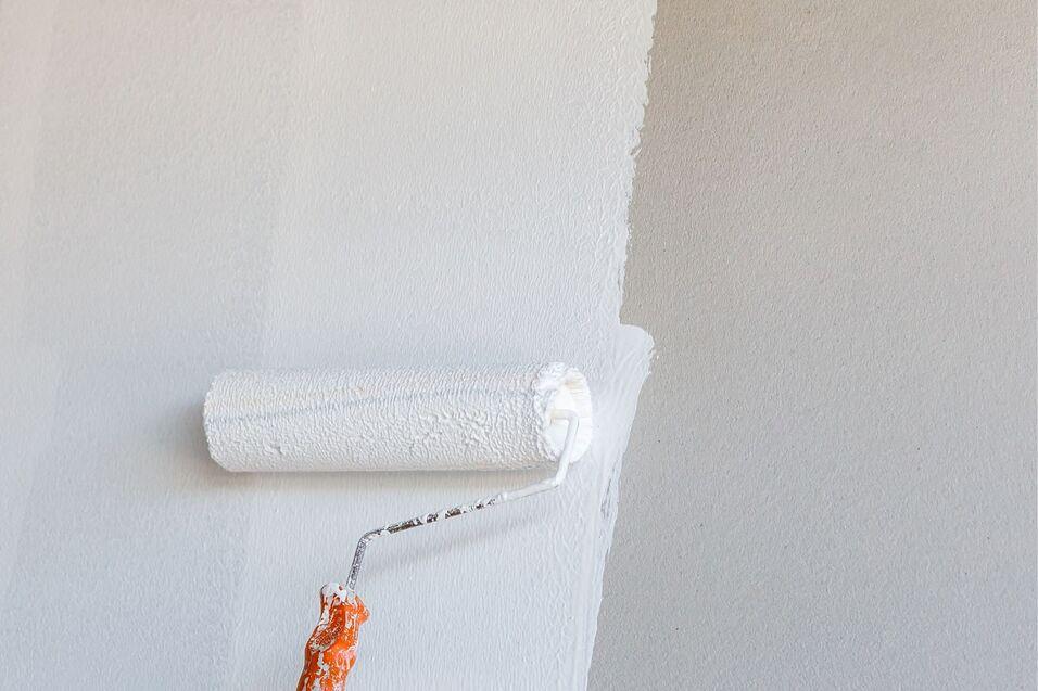 Farbroller mit orangefarbener Griff, der eine weiße Wand in einem hellen Raum streicht.