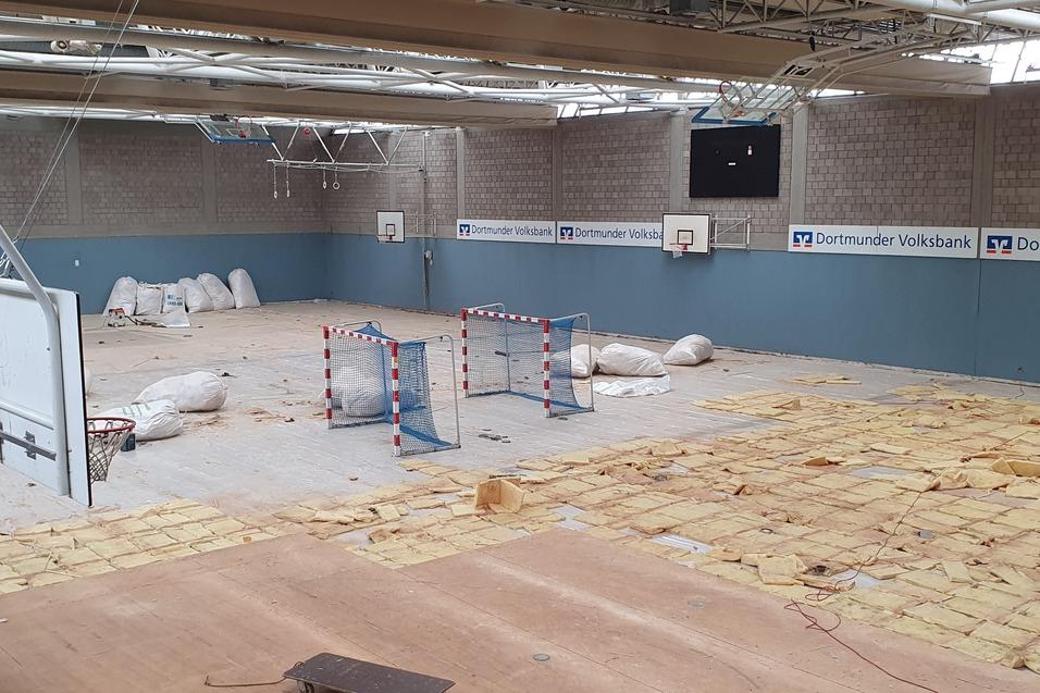 Leere Sporthalle mit einem Boden aus gelben Matten, zwei Toren und mehreren Deckenmaterialien in der Ecke.