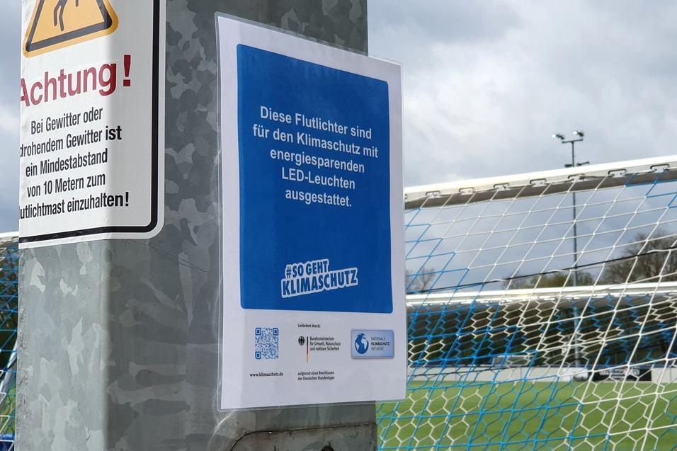 Hinweisblatt über energieeffiziente LED-Beleuchtung an einem Fußballtor auf einem Sportplatz.