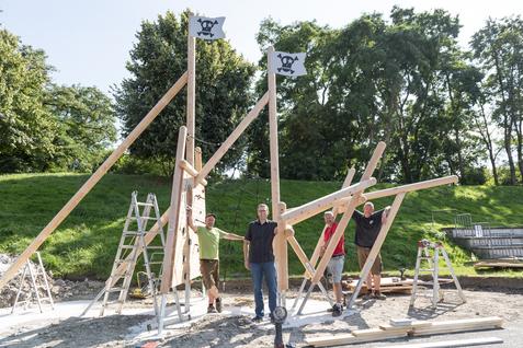 Bauarbeiter stehen neben frisch errichteten Holzpiratenflaggen auf einem Baugelände im Freien.