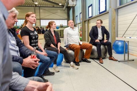 Fünf Personen sitzen auf Gymnastikbällen in einem Raum, diskutieren und schauen aufmerksam auf einen Sprecher.