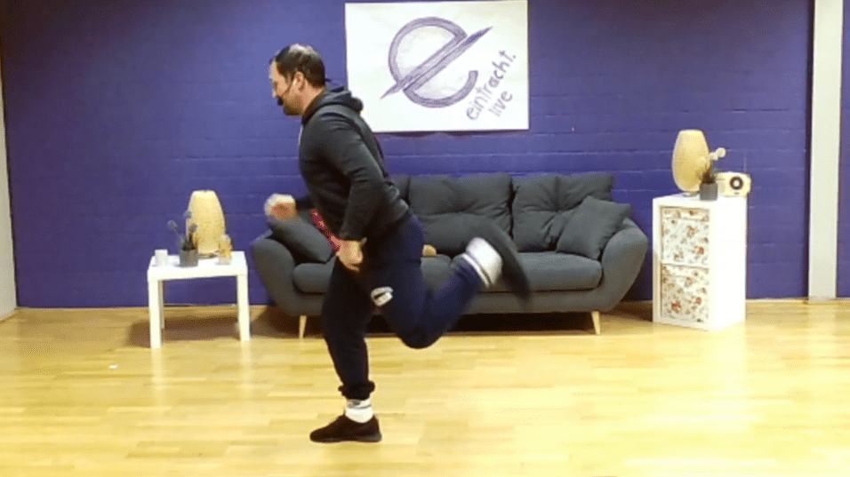 Mann in Sportkleidung führt eine Übung mit einer Hantel in der Hand in einem Fitnessraum aus.