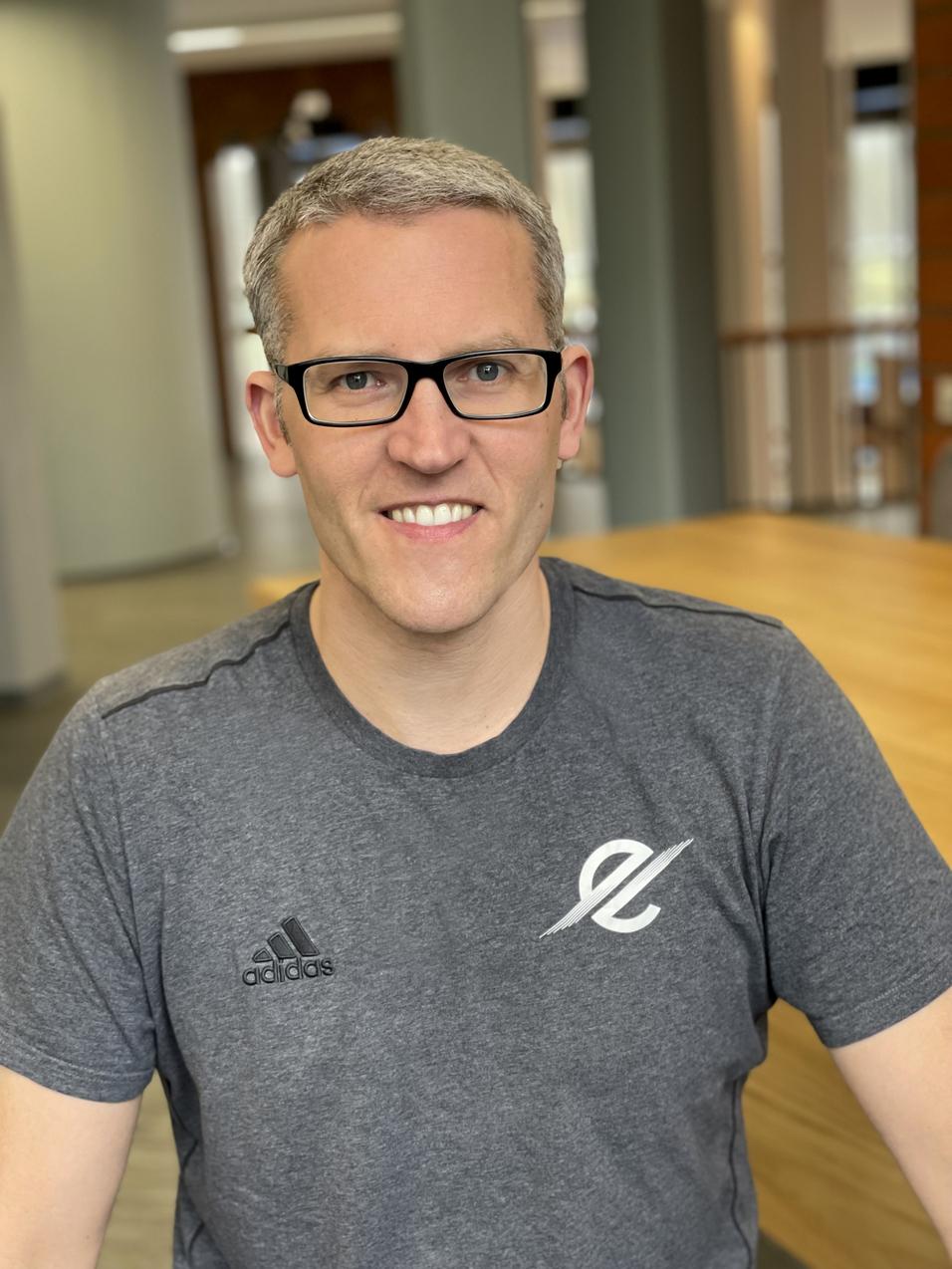 Mann mit Brille und grauem Sportshirt sitzt an einem Tisch in einem hellen Raum.