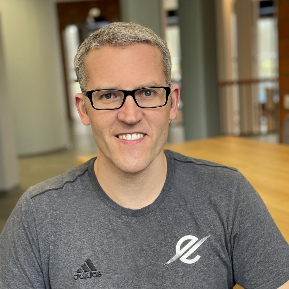 Mann mit Brille und grauem Sportshirt sitzt an einem Tisch in einem hellen Raum.