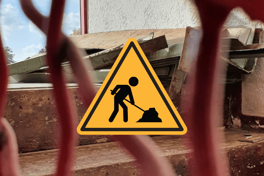 Warnschild f&uuml;r Baustelle mit Arbeiter, im Hintergrund Bauabf&auml;lle und Fenster sichtbar, durch Sicherheitsnetz fotografiert.