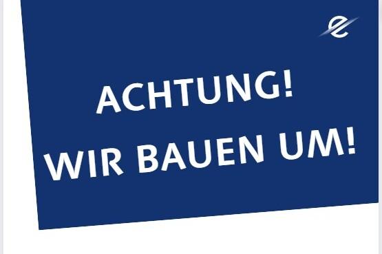 Blaues Schild mit dem Text &bdquo;ACHTUNG! WIR BAUEN UM!&ldquo; in wei&szlig;er Schrift.