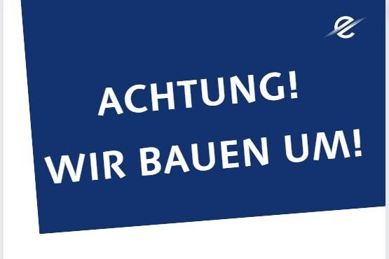 Blaues Schild mit dem Text &bdquo;ACHTUNG! WIR BAUEN UM!&ldquo; in wei&szlig;er Schrift.