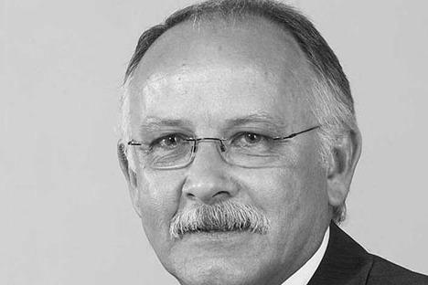 Schwarz-wei&szlig;-Portr&auml;t eines Mannes mit Brille und Schnurrbart, der einen Anzug tr&auml;gt und in die Kamera blickt.