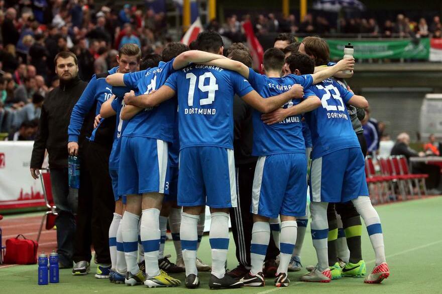 Gruppenumarmung von Fußballspielern in blauen Trikots mit der Aufschrift „Dortmund“ auf einem Sportfeld.