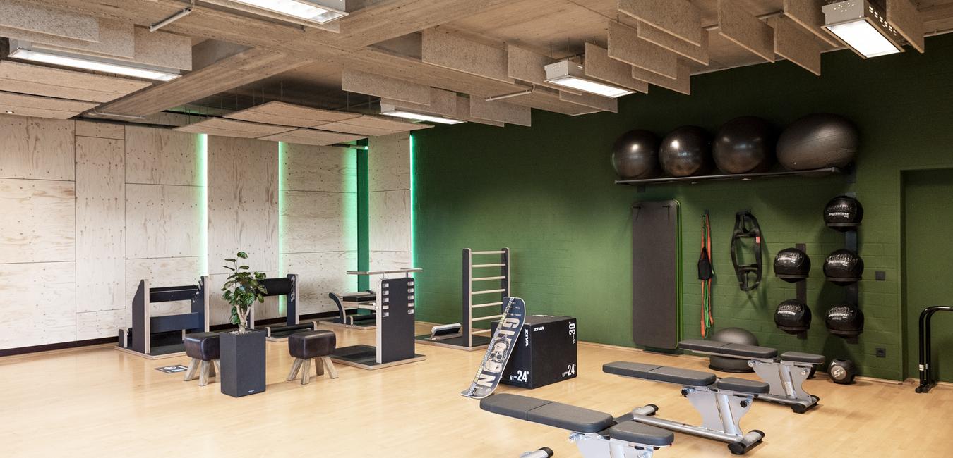 Fitnessraum mit Trainingsgeräten, Gewichten und einem spiegelnden Boden, grüne Wände und gut beleuchtet.