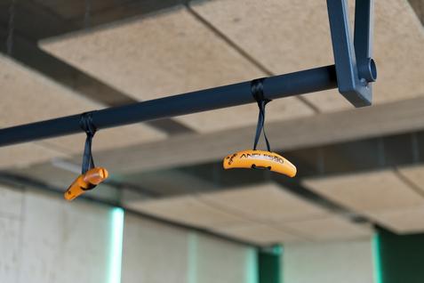 Zwei orangefarbene Griffleinen hängen an einer schwarzen Halterung in einem modernen Indoor-Trainingsbereich.