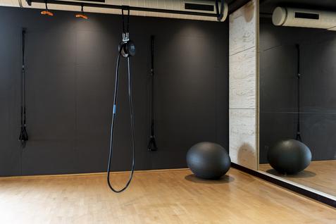 Blick in einen Fitnessraum mit Wandhalterungen, einem Gymnastikball und einem großen Spiegel.