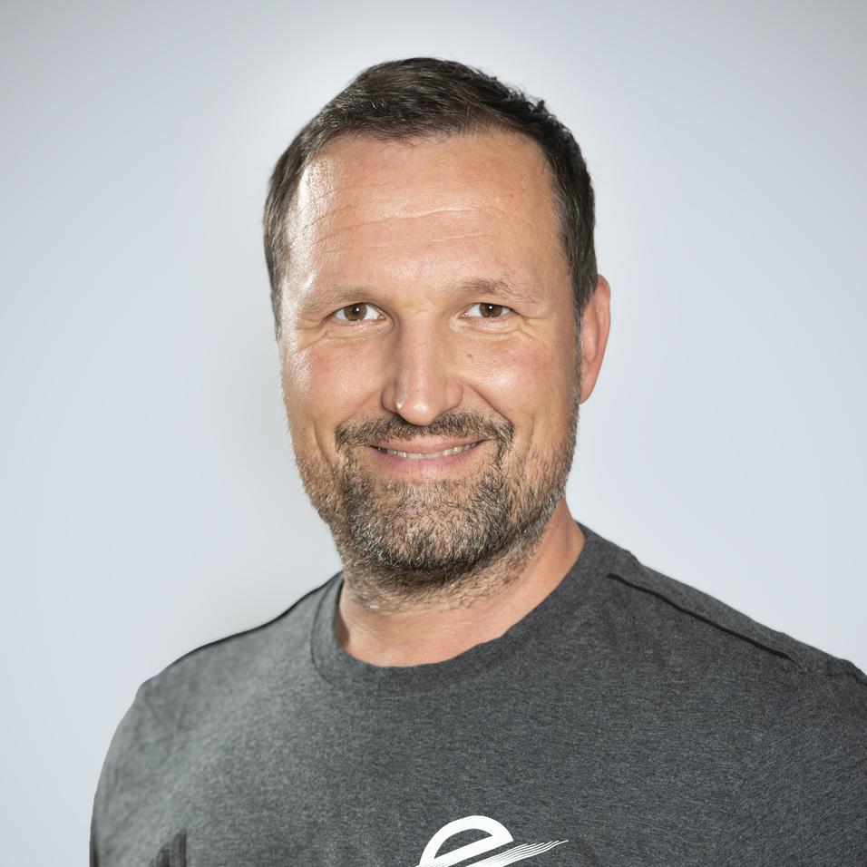 Portr&auml;t eines l&auml;chelnden Mannes mit kurzem, braunem Haar in einem grauen T-Shirt auf hellem Hintergrund.