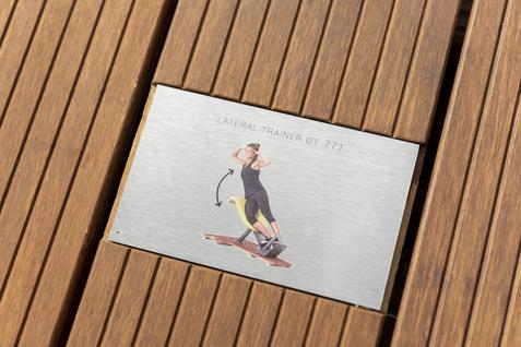 Schild mit Anleitung f&uuml;r den Lateral-Trainer 771, zeigt eine Person bei der &Uuml;bung auf einem Holzfu&szlig;boden.