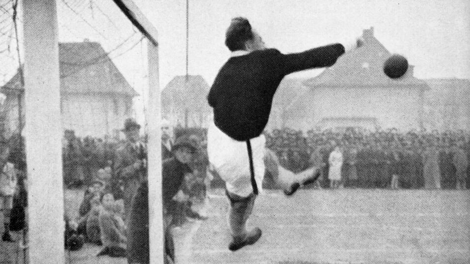 Ein Torwart springt nach einem Ball, vor einer Menge Zuschauer auf einem Fußballfeld.