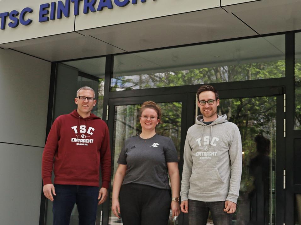 Drei Personen stehen vor dem Eingang des TSC Eintracht Dortmund, mit dem Logo und Schriftzug gut sichtbar.