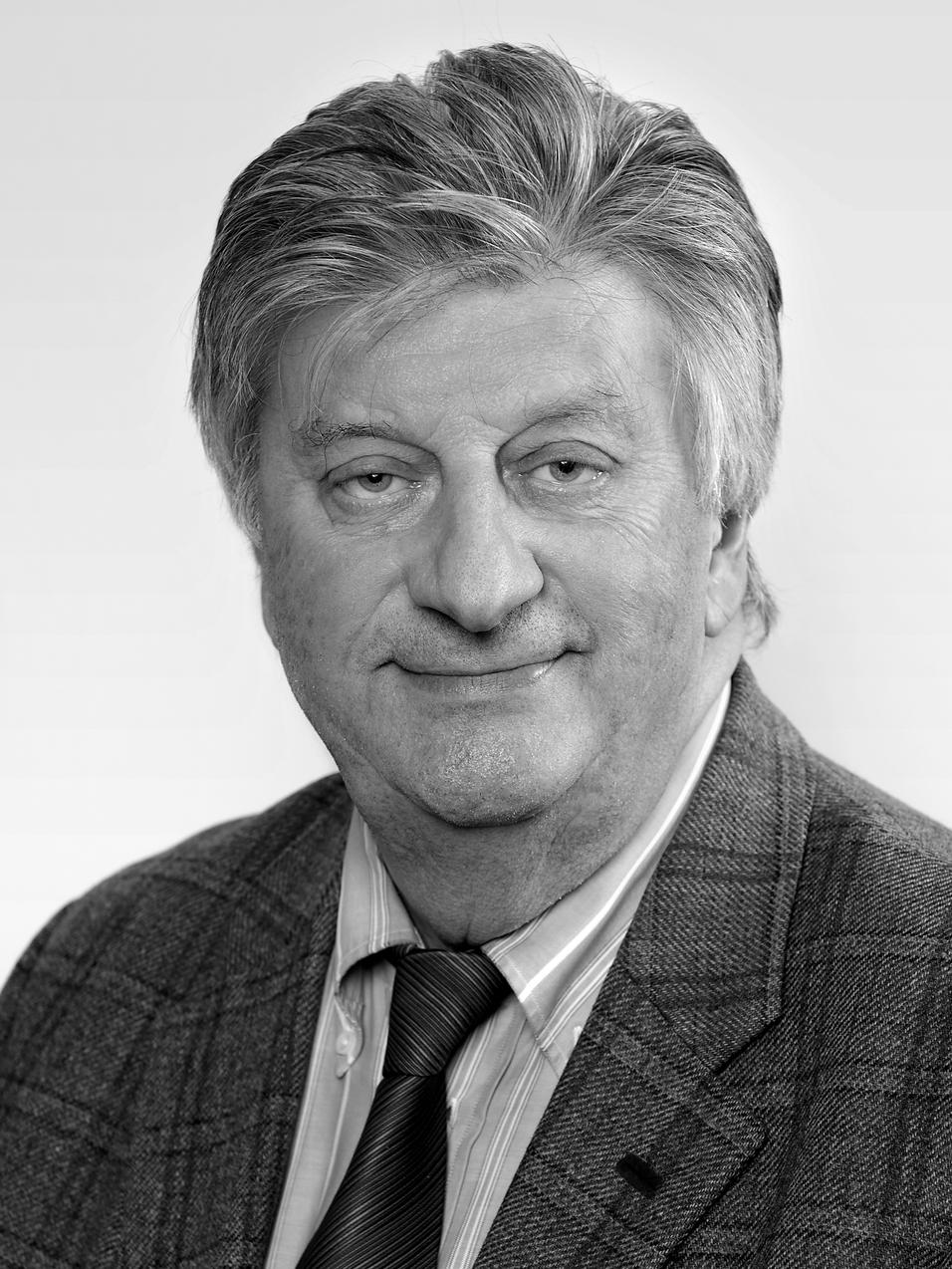 Schwarzwei&szlig;portr&auml;t eines &auml;lteren Mannes mit grauen Haaren, Anzug und Krawatte, freundlich in die Kamera l&auml;chelnd.