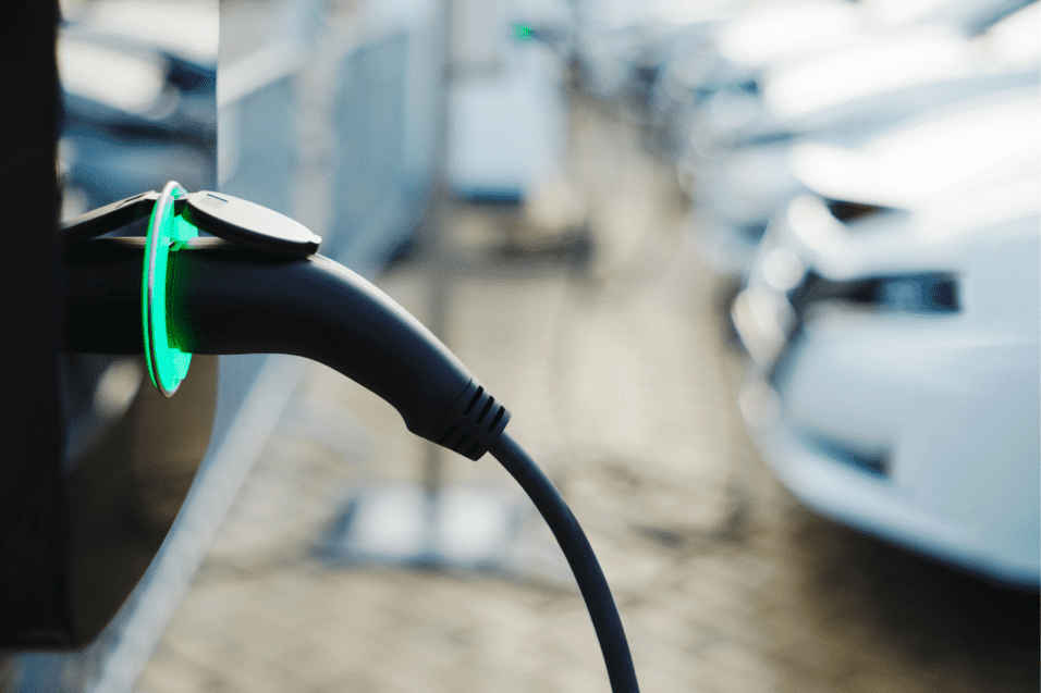 Ladekabel einer Elektroauto-Ladestation mit grünem Licht, im Hintergrund stehen mehrere parkende Autos.