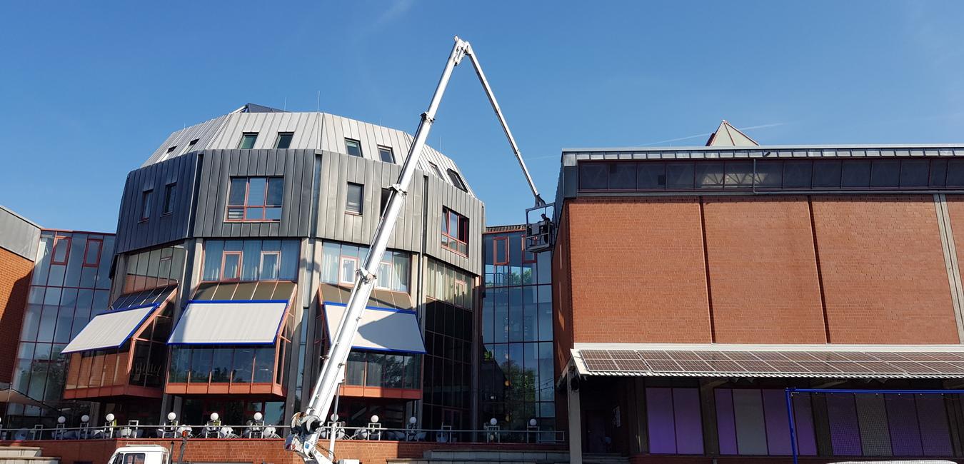 Blick auf ein modernes Geb&auml;ude mit Kran, der an der Fassade arbeitet, unter blauem Himmel.