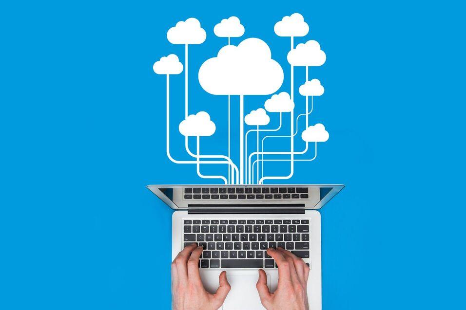 Laptop mit ge&ouml;ffnetem Deckel, H&auml;nde tippen, dar&uuml;ber sind Wolken und Datenleitungen auf blauem Hintergrund dargestellt.