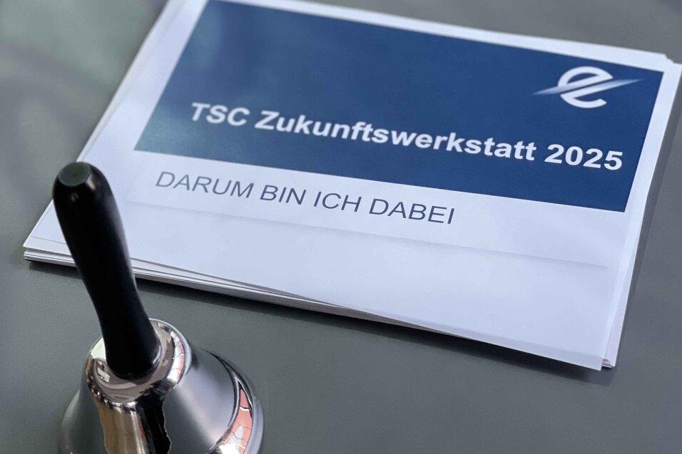 Detailaufnahme einer Tischglocke neben einem Informationsblatt zur TSC Zukunftswerkstatt 2025.