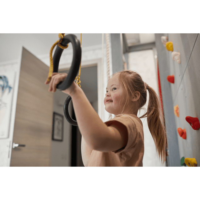 Mädchen mit Down-Syndrom hält an Turnringen in einem Spielzimmer, im Hintergrund eine Kletterwand.