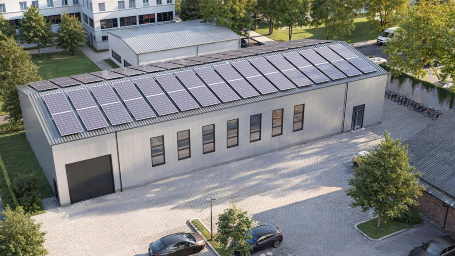 Moderne Lagerhalle mit Solarpanelen auf dem Dach, umgeben von B&auml;umen und Parkpl&auml;tzen.