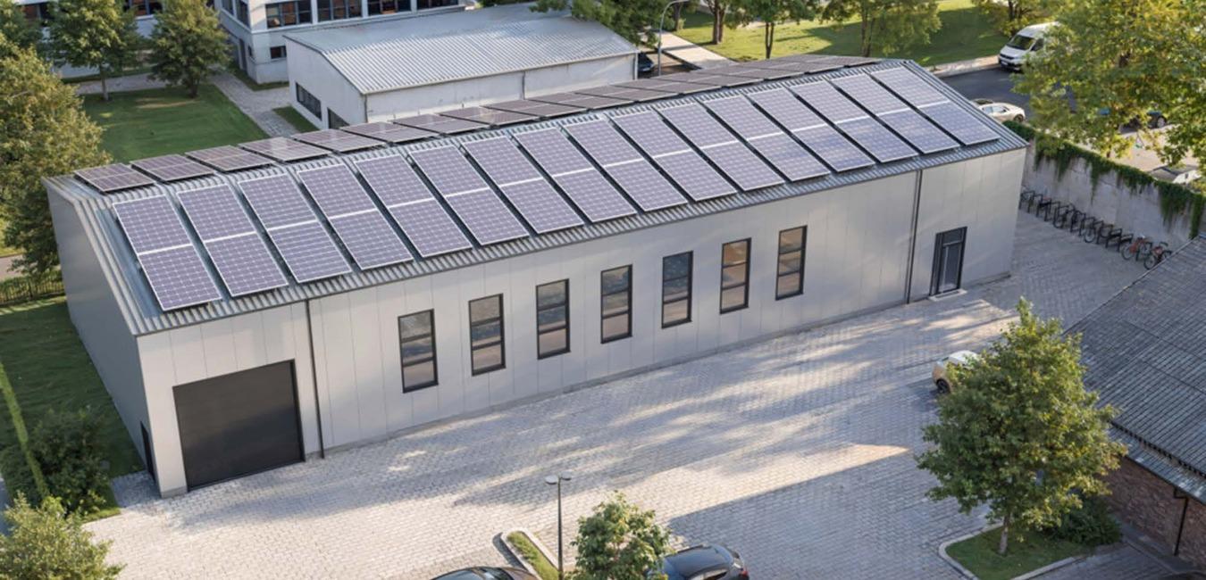 Moderne Lagerhalle mit Solarpanelen auf dem Dach, umgeben von B&auml;umen und Parkpl&auml;tzen.