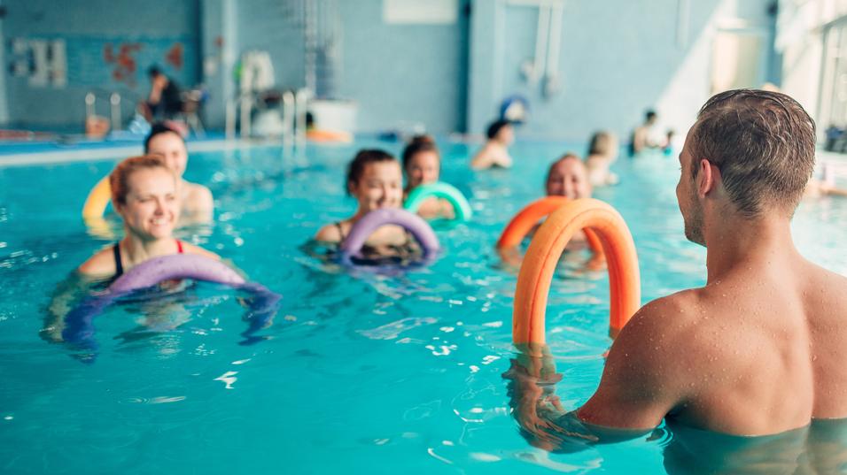 Gruppen von Schwimmern im Wasser nutzen Schwimmnudeln in einem hellblauen Schwimmbad während einer Übungssitzung.